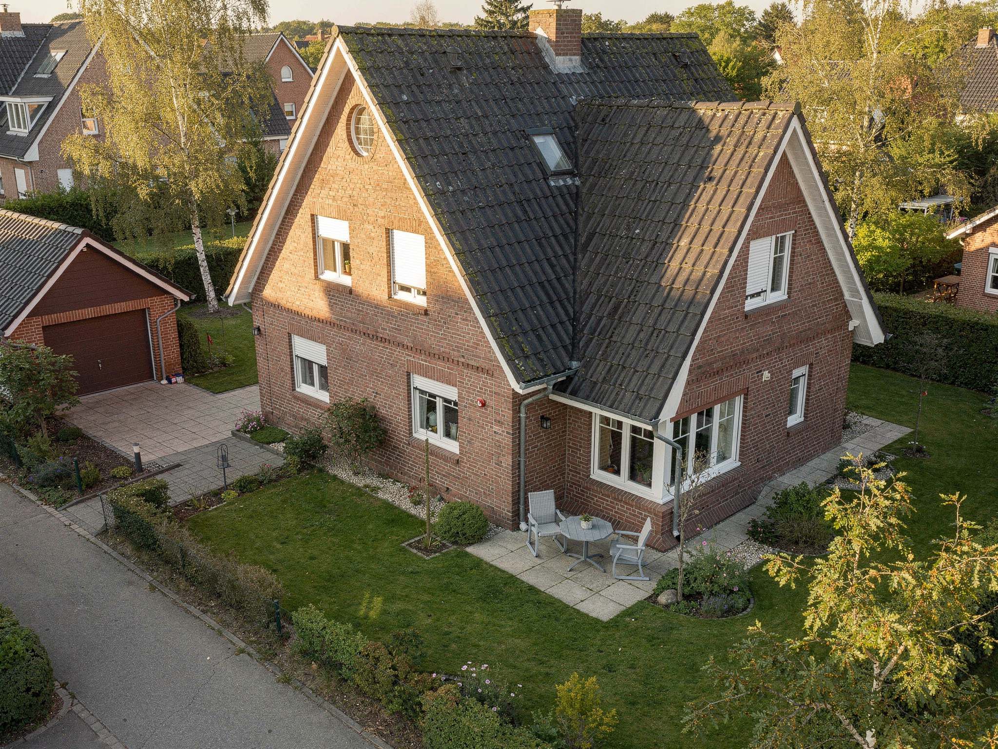 Schrägluftbild eines Klinker-Einfamilienhauses mit Garage, Terrasse und Garten im Abendlicht